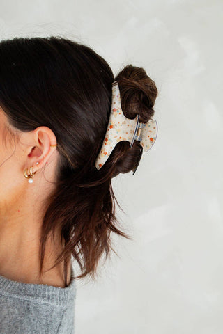 Person with a bun held in place by a decorative hair clip on a plain background