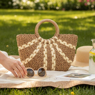 Woven handbag on a picnic blanket with sunglasses and a hat in a park setting