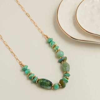 Necklace with green beads and gold chain on a light background