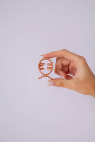 Hand holding a small, circular object with a design on a light purple background