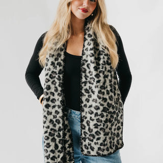 Woman wearing a leopard print scarf over a black top and jeans on a plain background