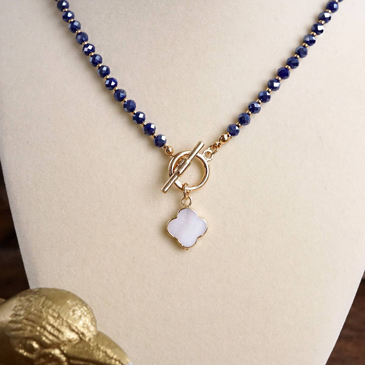 Necklace with blue beads and a white pendant on a mannequin bust, with a gold duck figurine in the foreground.