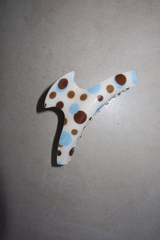 A white hair claw clip decorated with brown, light blue, and medium brown polka dots, shown against a neutral gray background.