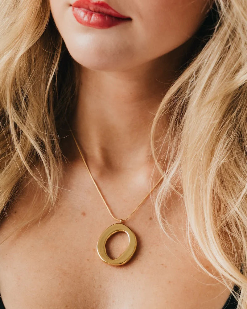 Close-up of a woman wearing a gold necklace with a circular pendant.
