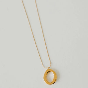 Gold necklace with a large oval pendant on a light gray background
