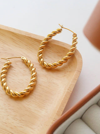 Gold hoop earrings on a wooden tray with a white background