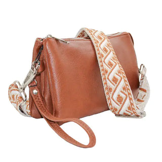 Brown leather handbag with a patterned strap on a white background