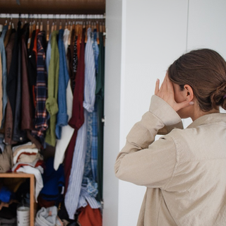 Woman standing in front of an open closet filled with clothes, holding her head in frustration.