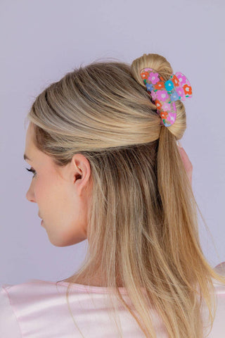 Woman with blonde hair styled in a bun with colorful hair accessories against a light purple background