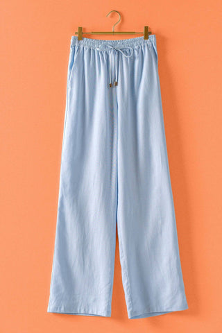Light blue pants hanging on a wooden hanger against an orange background