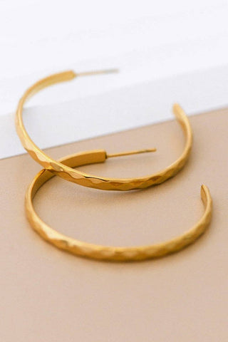 Gold hoop earrings on a beige surface with a white background