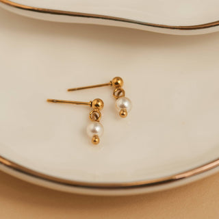 Gold and pearl earrings on a beige surface