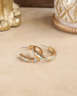 Gold hoop earrings with turquoise stones on a beige surface