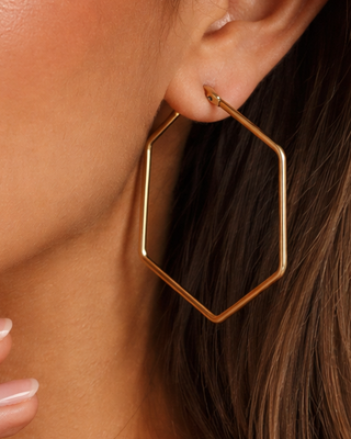 Gold hexagonal hoop earring worn by a person with dark hair.
