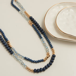 Blue beaded necklace with gold accents on a light surface with white plates in the background