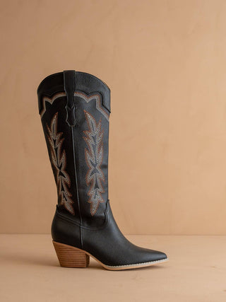 Black cowboy boot with brown heel on a beige background