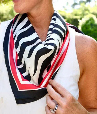 A woman outdoors wearing a white sleeveless top and a black, white, and red striped scarf.