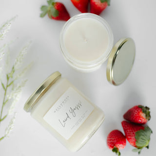 Candle jar with a gold lid and strawberry flavor label, surrounded by strawberries on a light background