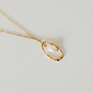 Gold necklace with a teardrop-shaped pendant on a light gray background