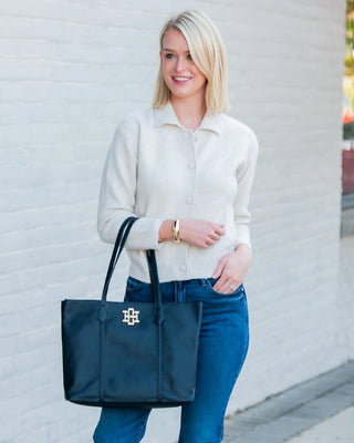 Woman holding a navy tote bag with a logo against a light gray wall