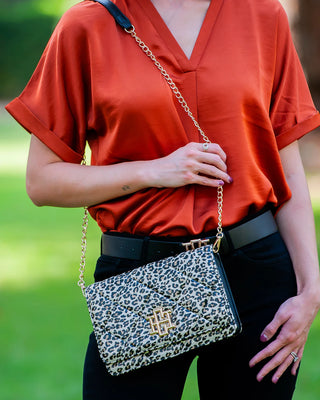Person wearing an orange shirt and holding a leopard print handbag outdoors.