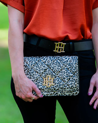 Person holding a leopard print clutch with gold accents, wearing a red top and black pants.