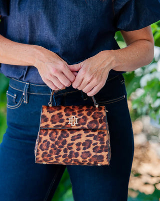 Person holding a leopard print handbag with a blurred natural background